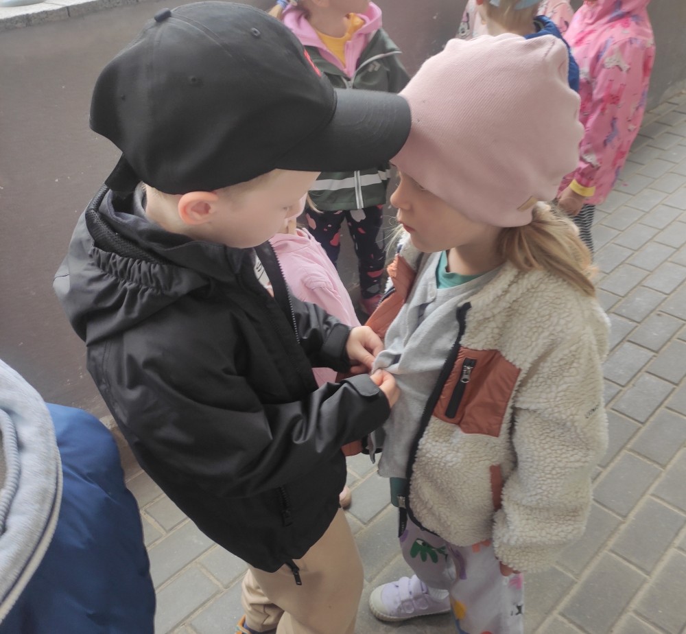 Małe dzieci pomagają sobie nawzajem zapinać kurtki przed wyjściem na dwór